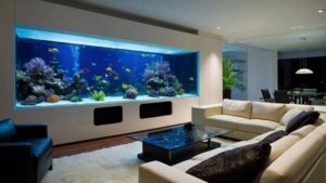 A modern living room features a large aquarium with colorful fish and corals beside a cozy seating area and elegant decor.